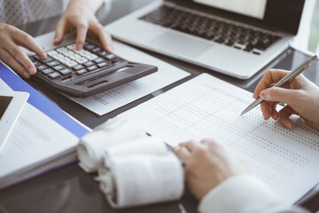 Woman accountant using a calculator and laptop computer while counting taxes for a client. Business audit concepts