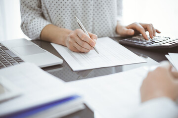 Woman accountant using a calculator and laptop computer while counting taxes for a client. Business audit concepts