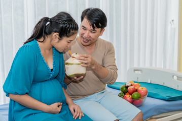 Asian family, husband holding a coconut for his wife who is 8 months pregnant to drink. to fruits...
