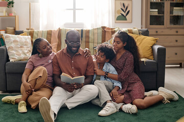Cheerful parents and children sitting on floor and reading Martin Luther King Jr biography