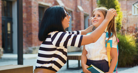 Mother helping and caring girl with bag outdoor near school building, education start and care for young student happy for class. Happy family back to school.