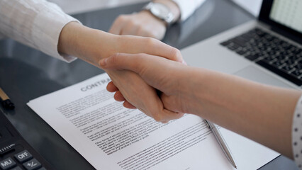 Business people shaking hands above contract papers just signed on the grey table, close up. Lawyers or entrepreneurs at meeting. Teamwork, partnership, success concept