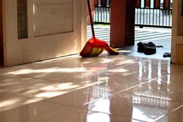 Foto auf Acrylglas interior of the house, in front of the door there is a floor that has been swept, there is a broom near the door with the front yard of the house in the background. © achmad anshori