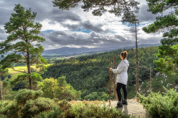Adult woman standing on the edge of cliff in Lead mines, admiring a view on a valley and pine forest below. Hiking in Wicklow Mountains, Ireland