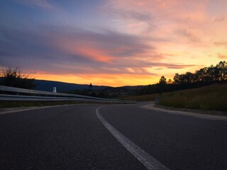 Sunset over an empty road surrounded by the silhouettes of hills and trees