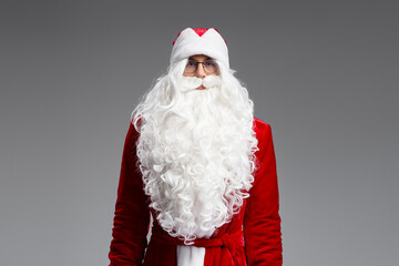 Portrait of Santa Claus with white beard wearing red costume looking at camera isolated on gray background. Happy New Year, Christmas holiday, winter season concept 
