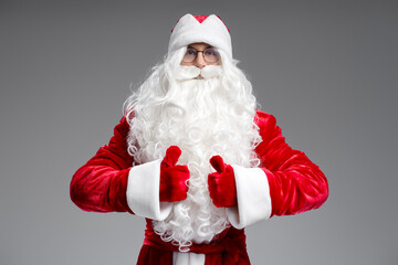 Portrait of Santa Claus holding thumbs up looking at camera isolated on gray background. Happy New Year, Christmas, holiday, winter concept