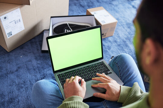 Online shopping, man with laptop, green screen and boxes on floor, shoes and delivery service on digital app. Sale, discount and ecommerce on fashion retail brand website, internet search on computer - Powered by Adobe