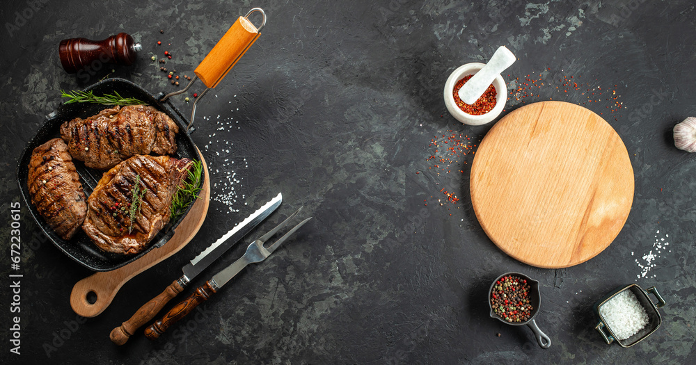 Wall mural marbled beef steaks in a grill pan with wine glass on a dark background. menu, recipe mock up, banne