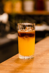  Bumble coffee with ice on a bar. Espresso, orange juice, syrup in layers in glass with ice. Refreshing coffee drink. Coffee house menu, recipe