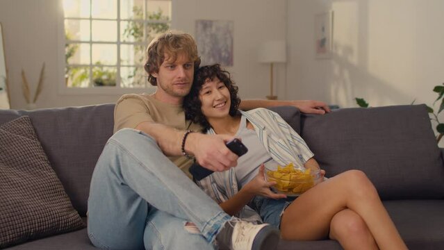 Medium shot of two young people in love starting watching TV show together while eating bowl of tachos