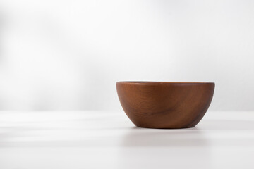 A vacant wooden bowl on the table and a white background in the morning.