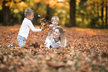 Fototapeta premium Happy young mother and two brothers walking in the autumn forest. Autumn outdoor activity for family with kids. Happy mothers day.