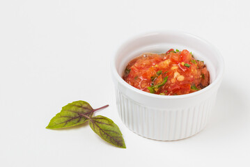 Tomato red sauce or vegetable dip in ceramic bowl with basil leaves isolated on white background