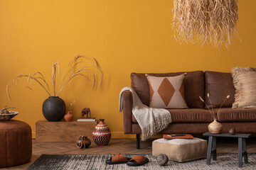 Warm and cozy living room interior with brown sofa, yellow wall, pillows, straw lamp, vase with...