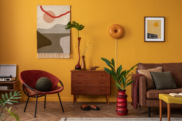 Aesthetic composition of warm and cozy living room interior with stylish kilim rug, wooden sideboard, plant, yellow wall, red armchair, brown sofa and personal accessories. Home decor. Template.