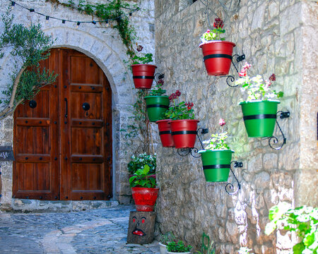 Red and green flower pots adorning the wall to an old wooden arched doorway in Berat, Albania