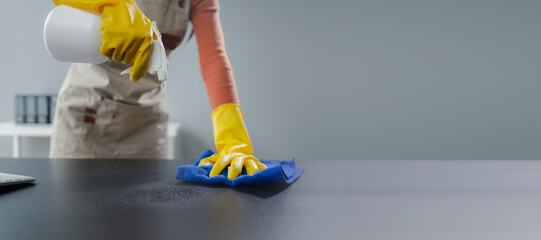 Cleaning desk surface in office with sanitizer spray, wear gloves and wipe the table with a towel,...