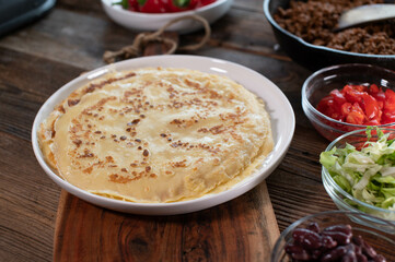 Mexican pancakes with meat, and ingredients on a wooden table