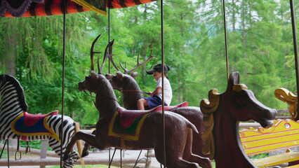 Happy small boy riding merry-go-round, rides carousel. Excited child having fun at circus festival,...