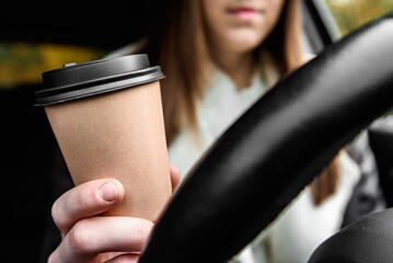 Woman holding steering wheel and paper cup with coffee.