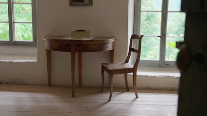 Rustic farmhouse setting, antique wooden table and chair by window in rural house