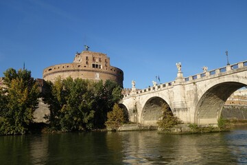 Arch bridge over a tranquil blue body of water, with a historical castle in the background