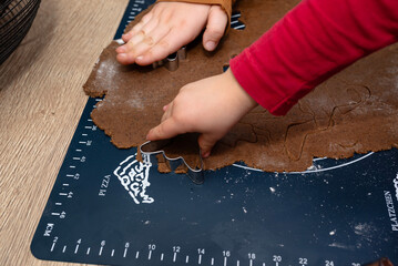 A child cutting out various shapes of gingerbread from raw dough using shapes.