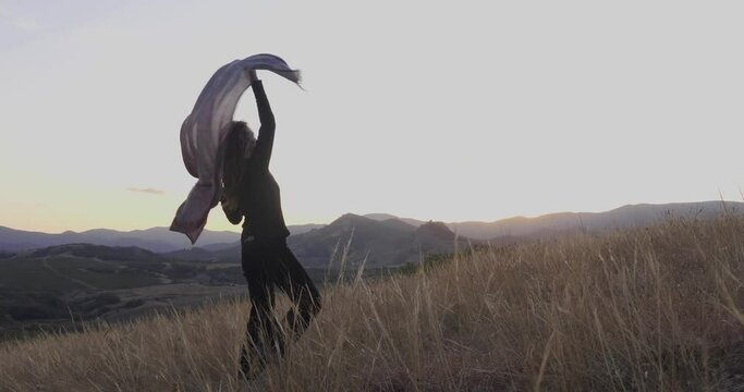 A woman in black clothes dances with a scarf against the backdrop of a mountain evening landscape. Symbolic personification of a psychological state. Psychology and health care