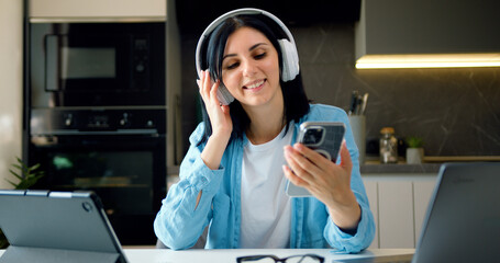 Happy relaxed woman freelancer dancing sitting at laptop wearing headphones listening music using...