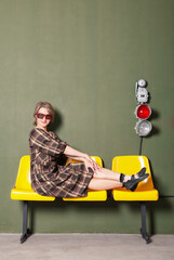 Beautiful woman wearing retro style checkered dress sitting on the yellow chairs