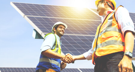 Caucasian male architect and Asian engineer electrician shaking hands working colleagues team believing positive approach planning solar power project solar panels success developing energy industry. - obrazy, fototapety, plakaty