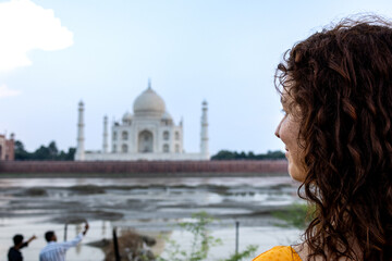 Woman looks at the imposing Taj Mahal in Agra, India, with its wonderful architecture on a cloudy...