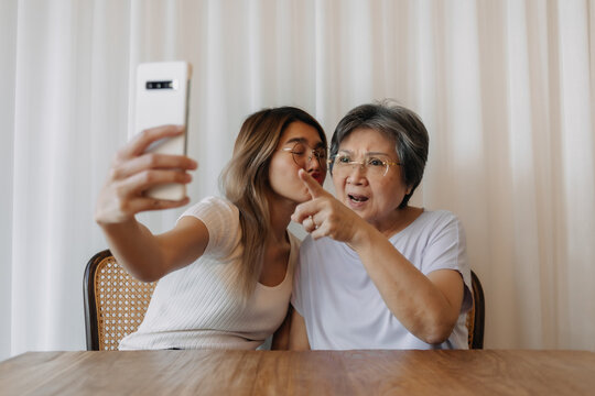 Asian Thai old mother and daughter using and holding phone, both woman looking at smartphone, taking selfie with happy smiling together, kissing mom.