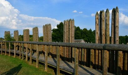 A close up on an old borough or village surrounded by a wooden palisade made out of logs, planks,...