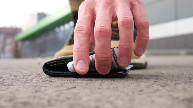 Close-up of a lost wallet on the asphalt with hundred dollar bills sticking out of it and a random person picking it up