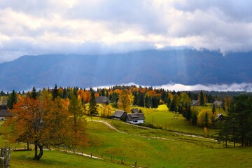 View of Uskovnica alpine pasture in Julian alps, Gorenjska, Slovenia with sunlight shining through the clouds and orange colored autumn trees
