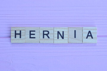 word hernia from small gray wooden letters lies on a pink wooden table