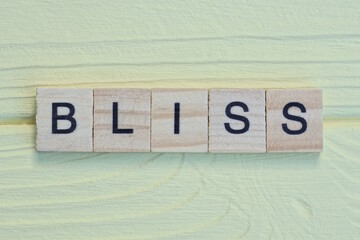 the word bliss of gray small wooden letters lies on a yellow wooden table