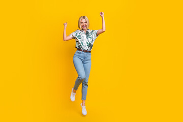 Full length photo of ecstatic overjoyed girl dressed print shirt jumping raising fists up win betting isolated on yellow color background