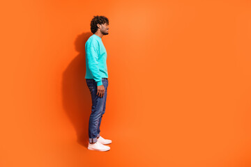 Full length side profile shot of arabian guy wearing casual outfit looking interested brands outlet isolated on orange color background