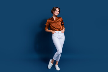 Fototapeta na wymiar Full length photo of lovely young lady hands pockets posing wear trendy brown blouse isolated on dark blue color background