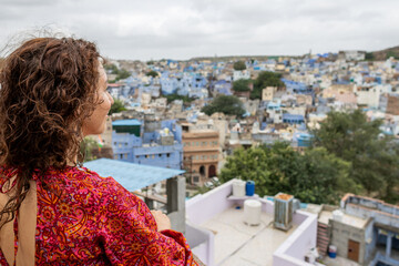 Woman dressed in red looking at the blue city from Mehrangarh Fort in Jodhpur in Rajasthan, India.