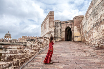 Woman dressed in red walking through Mehrangarh Fort in Jodhpur in Rajasthan, India. Known as the...