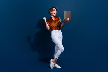 Full length photo of shiny lucky girl dressed brown shirt winning game modern device isolated blue...