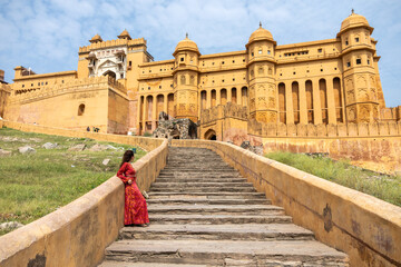 Woman at the entrance to Amber Fort in daytime with cloudy sky, near Jaipur, The Pink City,...