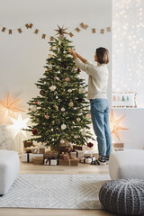 Young woman decorating Christmas tree at home, winter holiday and xmas time concept