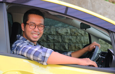 Adult Asian man smiling at the camera from inside his car - obrazy, fototapety, plakaty