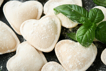 Italian ravioli pasta in heart shape. Tasty raw ravioli with flour and basil on dark background. Food cooking ingredients background. Valentines or Mothers Day lunch ideas. Top view with copy space.