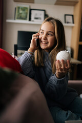 Vertical portrait of cute little girl talking on smartphone, holding in hand silver festive...